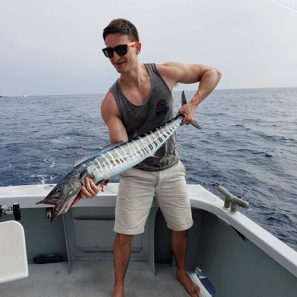 Kyle on a fishing boat, holding up a barracuda